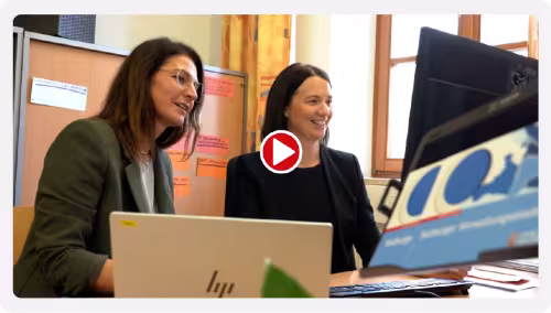 Video preview for the new LEMS learning platform: two employees sitting at a workstation in front of a laptop and monitor