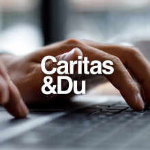 Hands typing on laptop keyboard, Caritas & Du logo visible